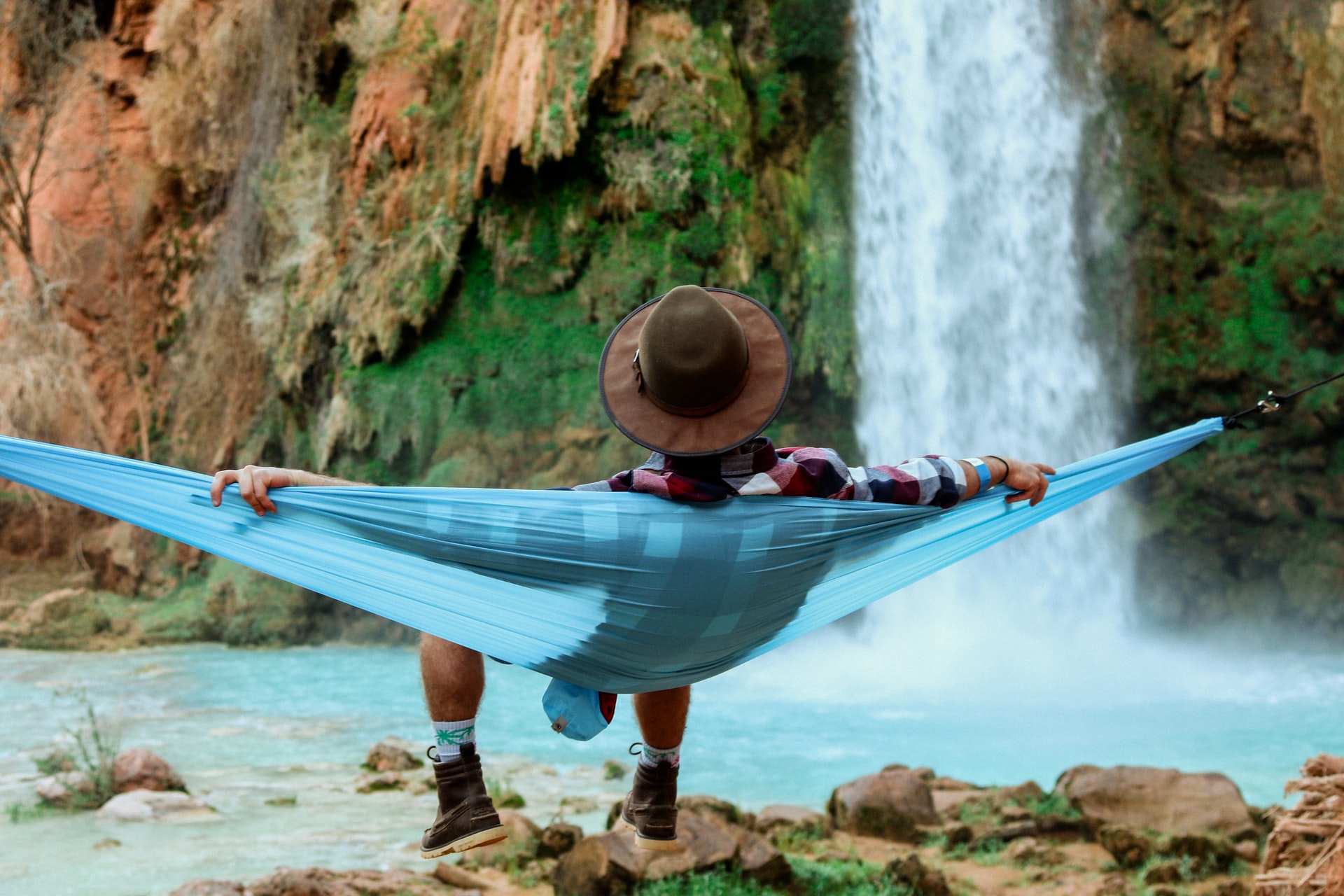 man sitting in a hammock looking at a waterfall